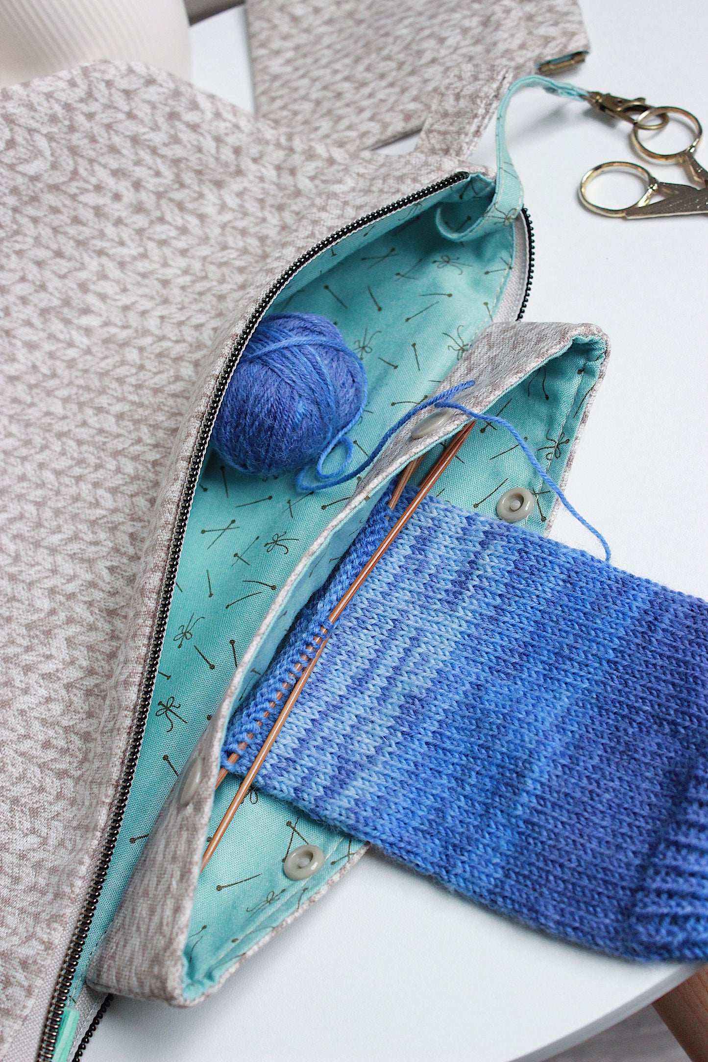 Beige knitting project bag showcasing blue yarn, knitting needles, and a DPN holder.