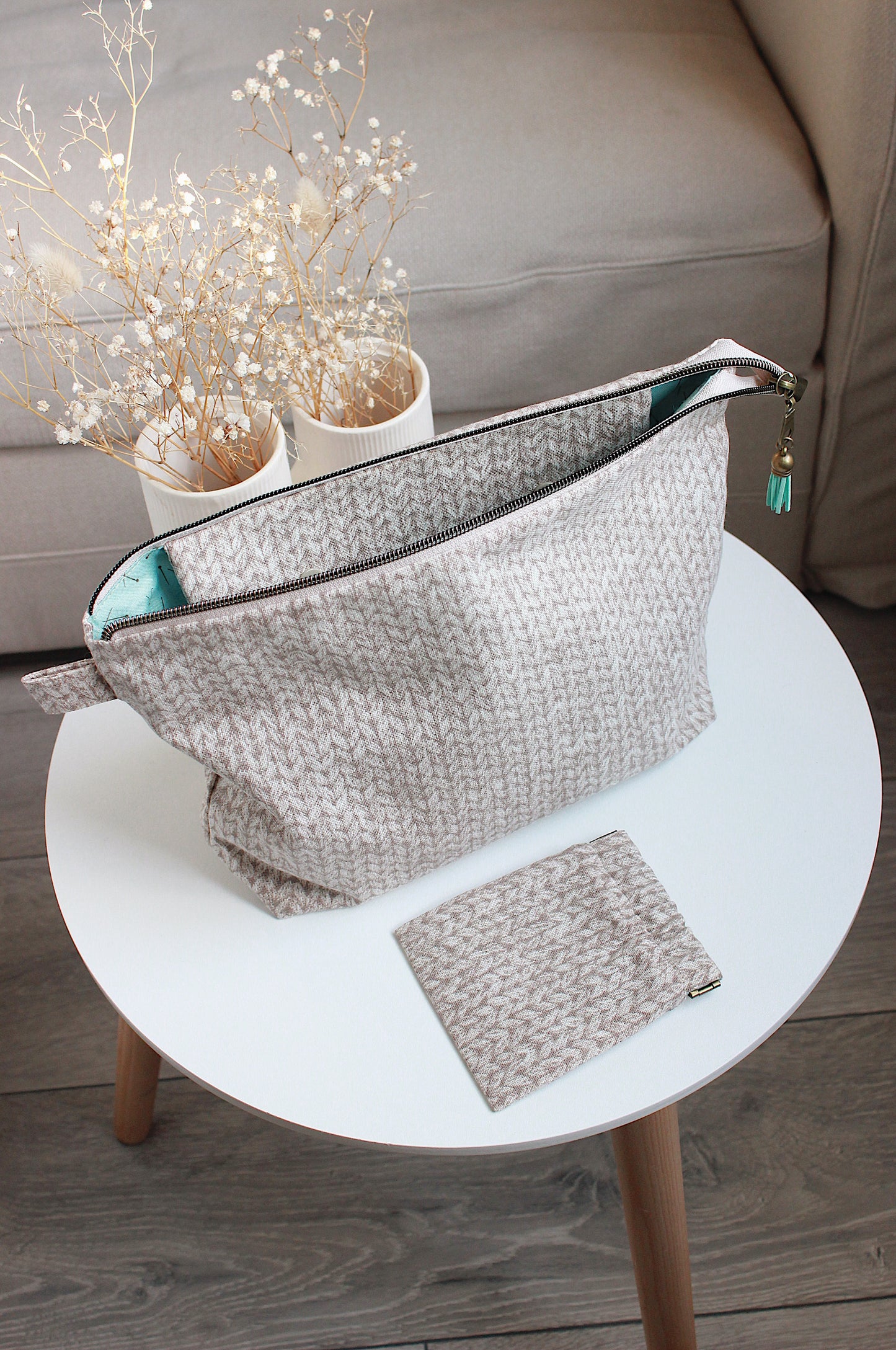 Beige knitting project bag with built-in DPN holder and matching squeeze purse on a white table with dried flowers.