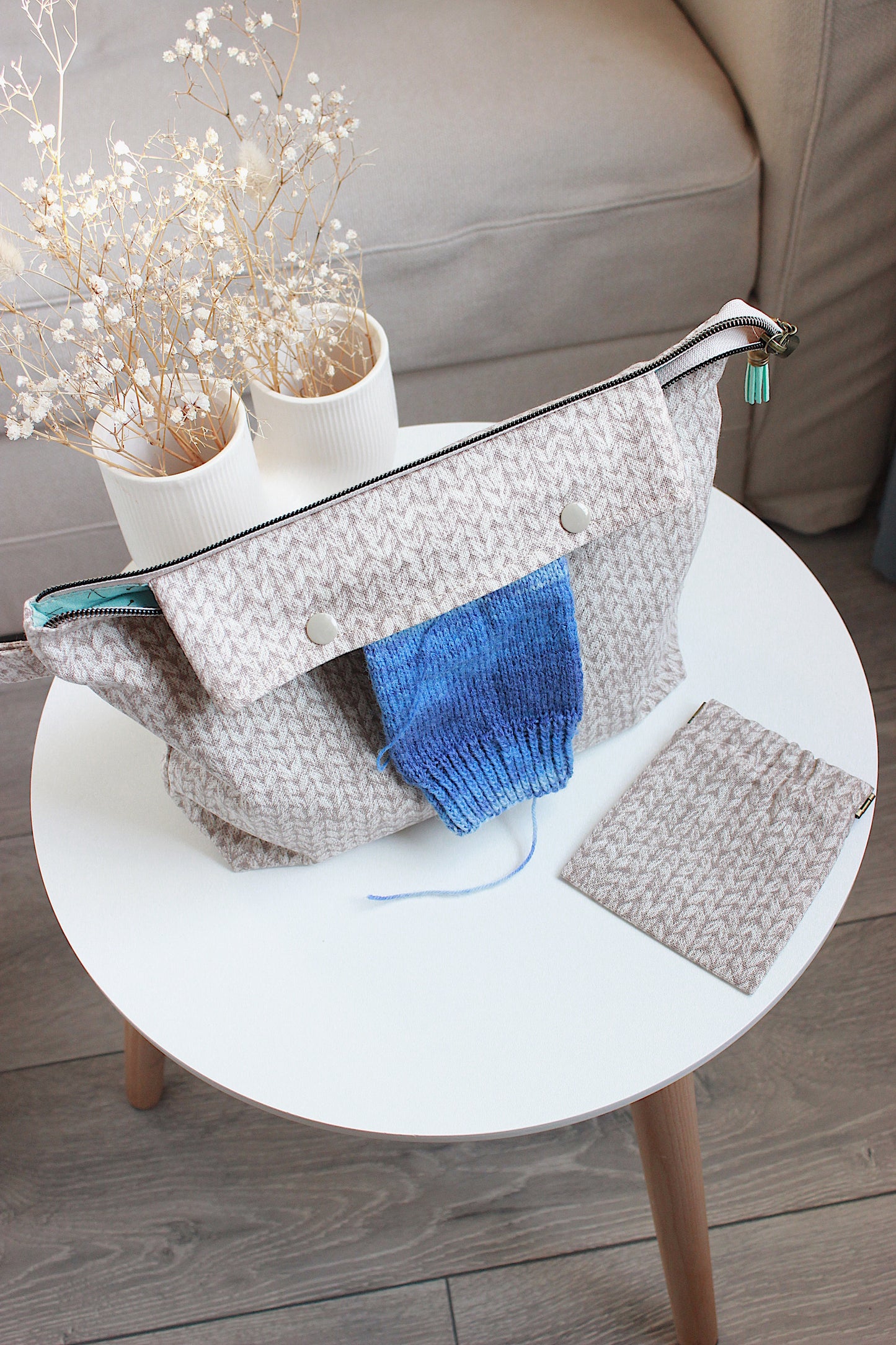 Beige knitting project bag with built-in DPN holder, blue yarn, and matching squeeze purse on a table.