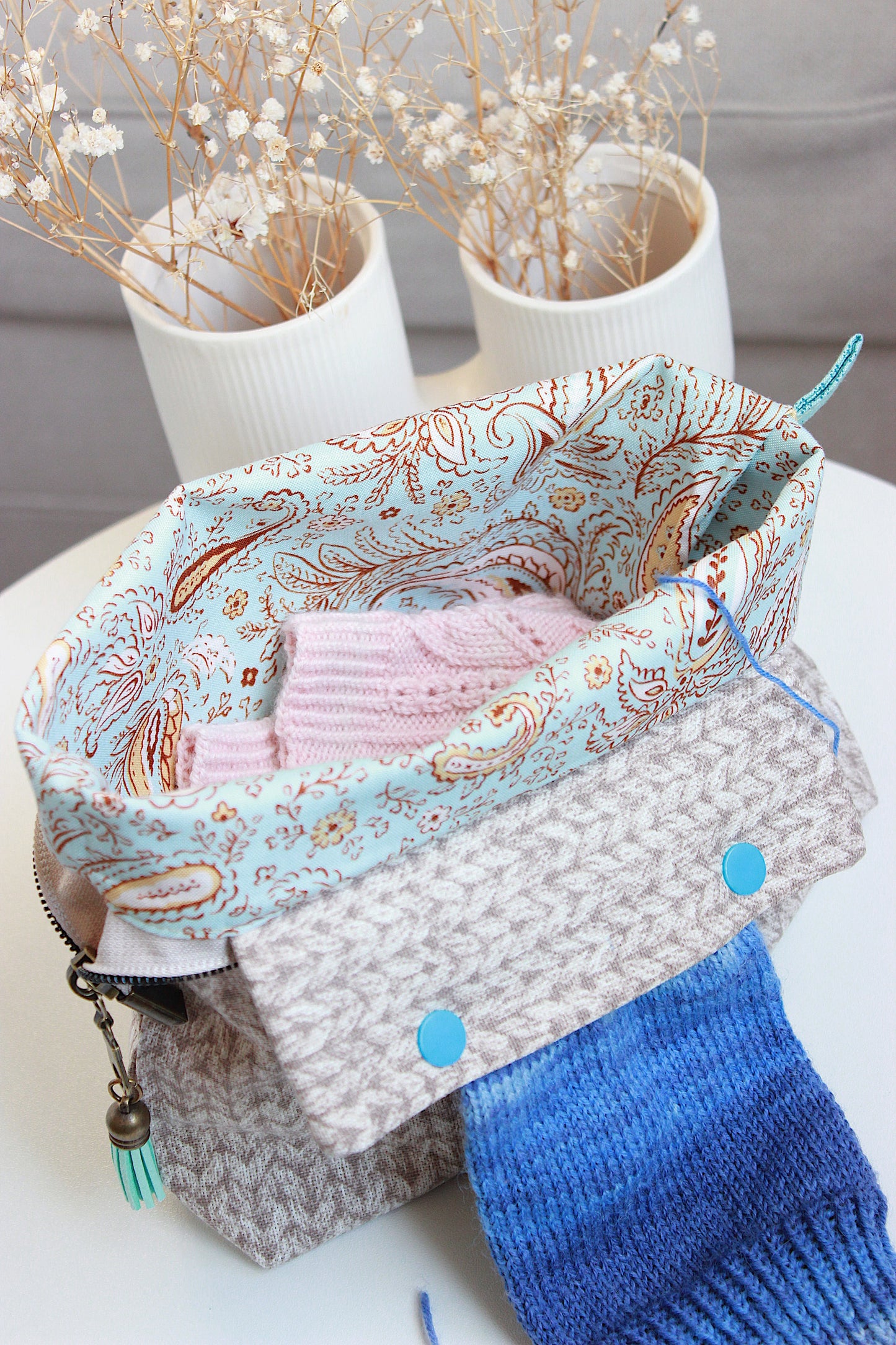 Beige knitting project bag with DPN holder, featuring a paisley pattern and colorful yarn peeking out.