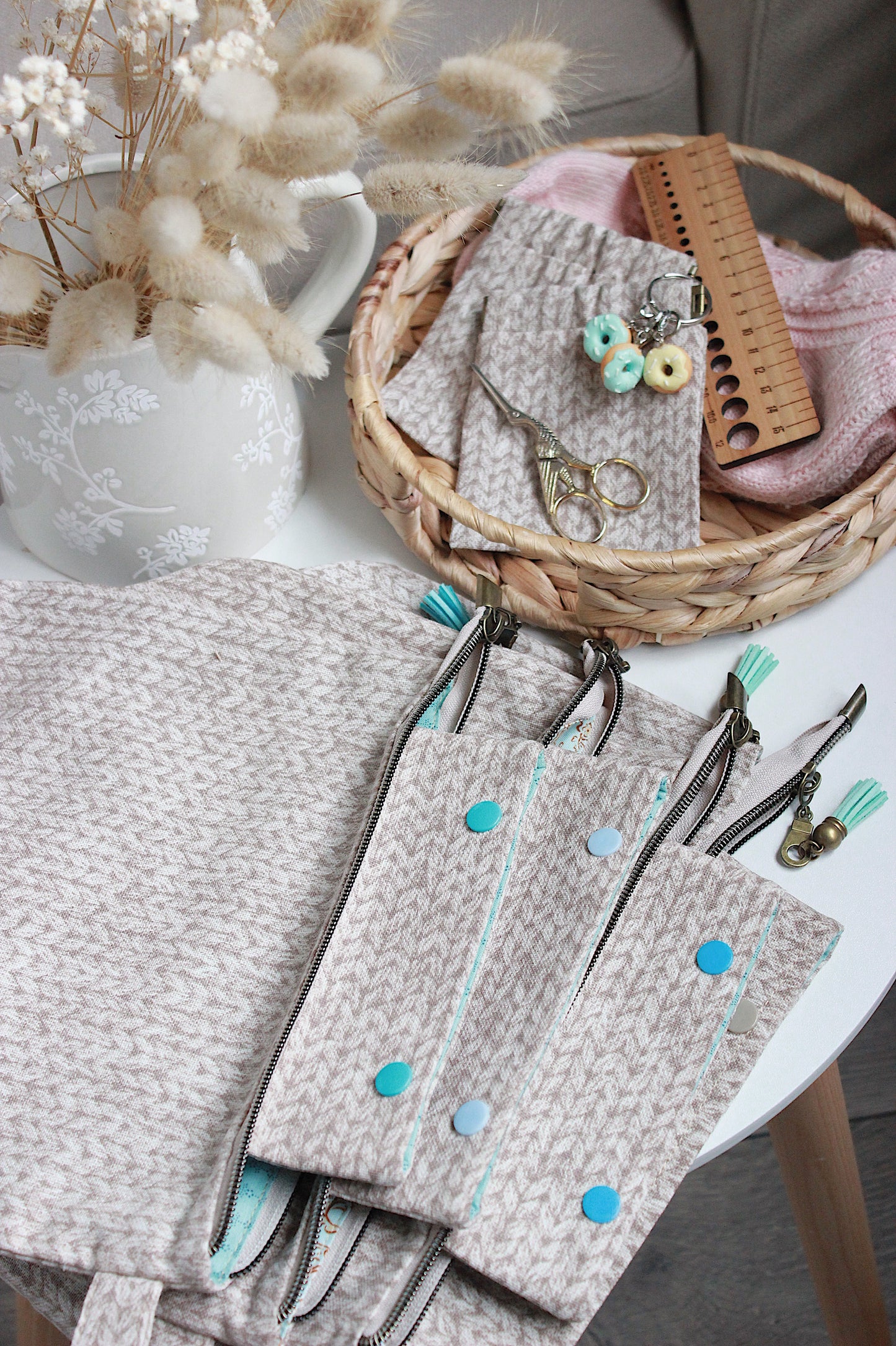 Beige knitting project bag with accessories including knitting tools and a basket of yarn organised on a table.