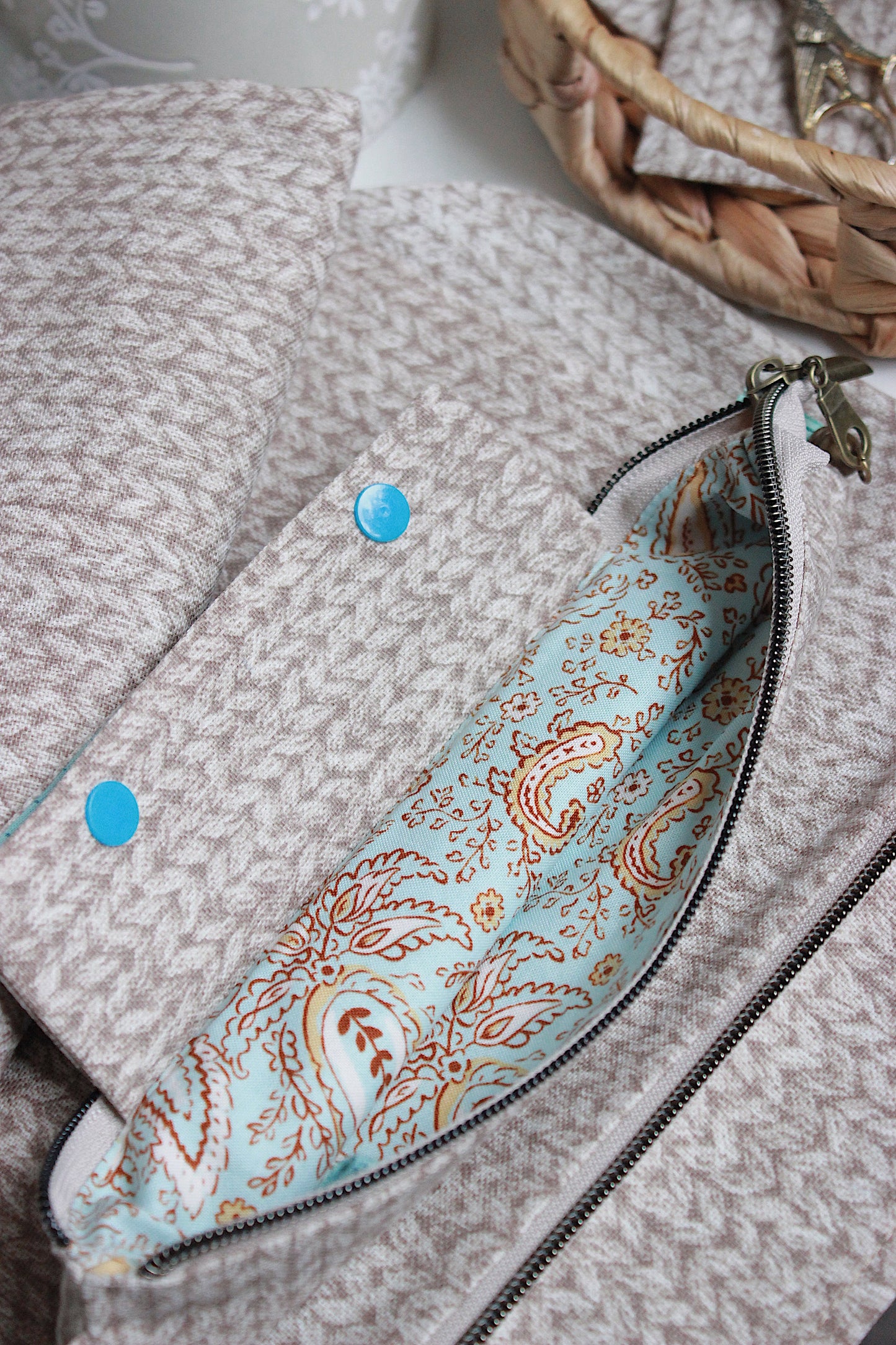 Close-up of beige knitting project bag featuring a zipper and colorful paisley lining.