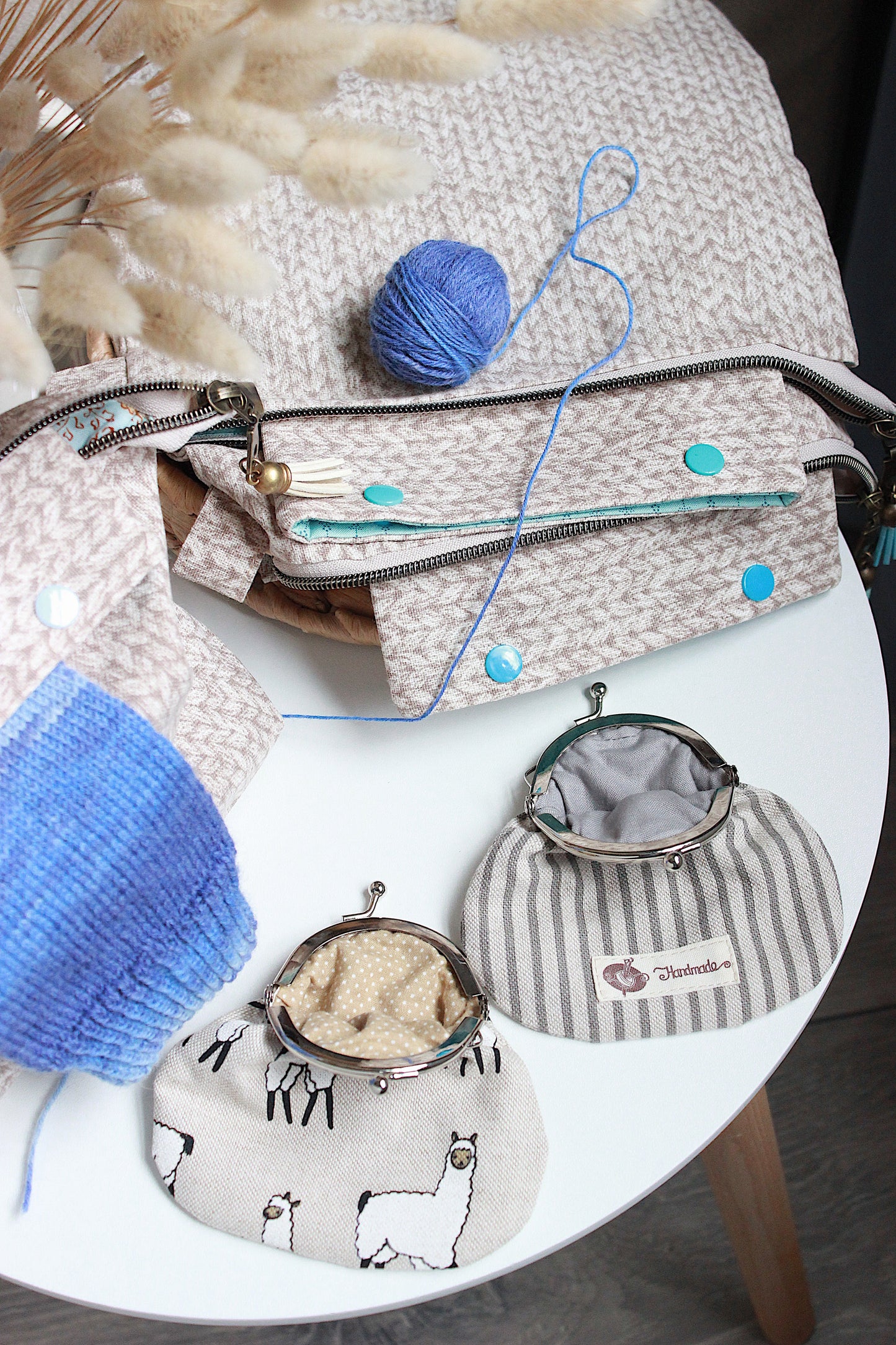 Beige knitting project bag with blue accents, DPN holder, and matching squeeze purses on a table with yarn.