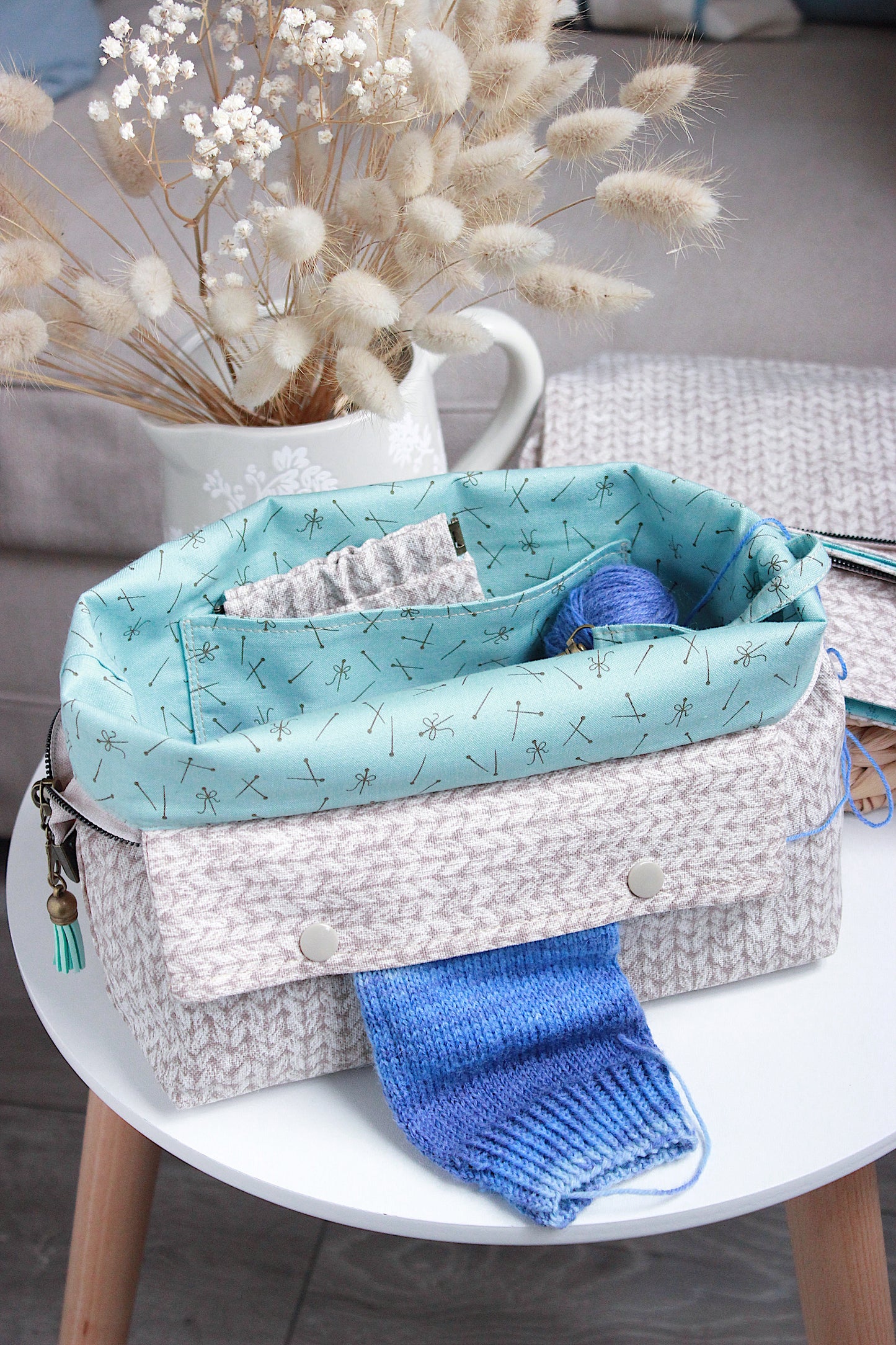 Beige knitting project bag with built-in DPN holder and colorful yarn inside, placed on a table with decorative elements.